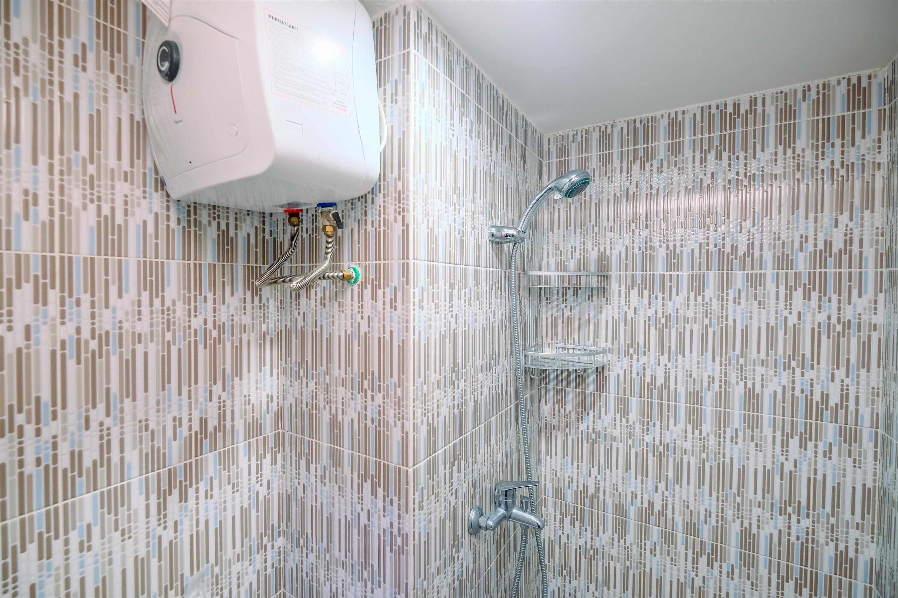 Een badkamer met een betegelde muur, een witte boiler en een douche met een chromen kraan.