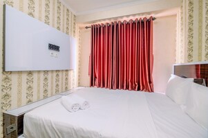 Una habitación de hotel con una cama, un televisor montado en la pared y una cortina roja.
