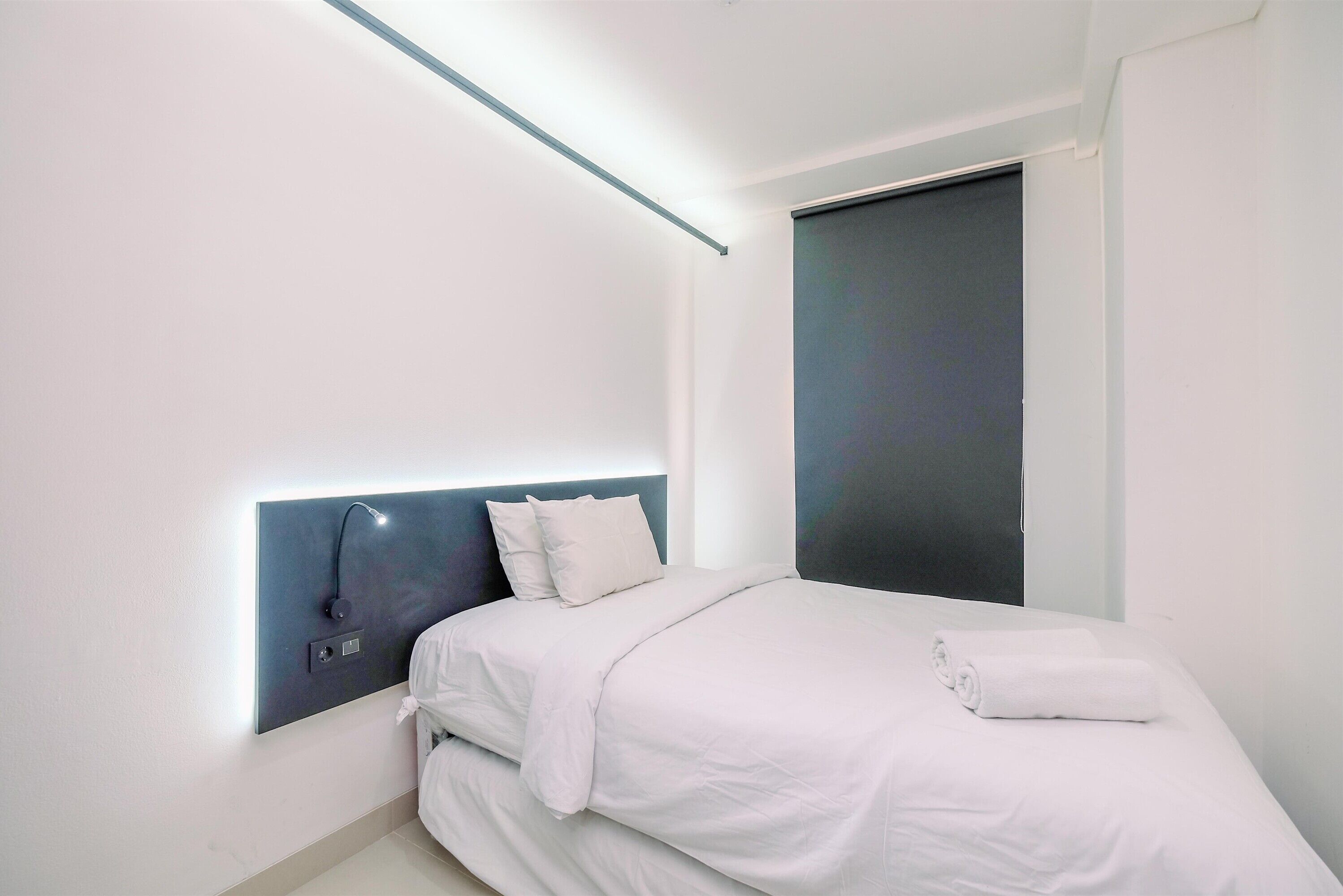 A modern bedroom with a bed, a headboard with built-in lighting, and a dark-colored door.