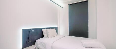 A modern bedroom with a bed, a headboard with built-in lighting, and a dark-colored door.