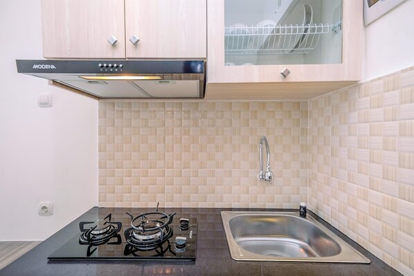 A modern kitchen with a black induction cooktop, a stainless steel sink, and wooden cabinets. - Well Designed and Comfy Studio at Podomoro Golf View Apartment (Gunung Putri)