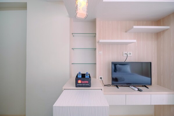 A modern hotel room with a flat-screen TV, a minibar, and a wall-mounted shelf. - Well Designed and Comfy Studio at Podomoro Golf View Apartment (Gunung Putri)
