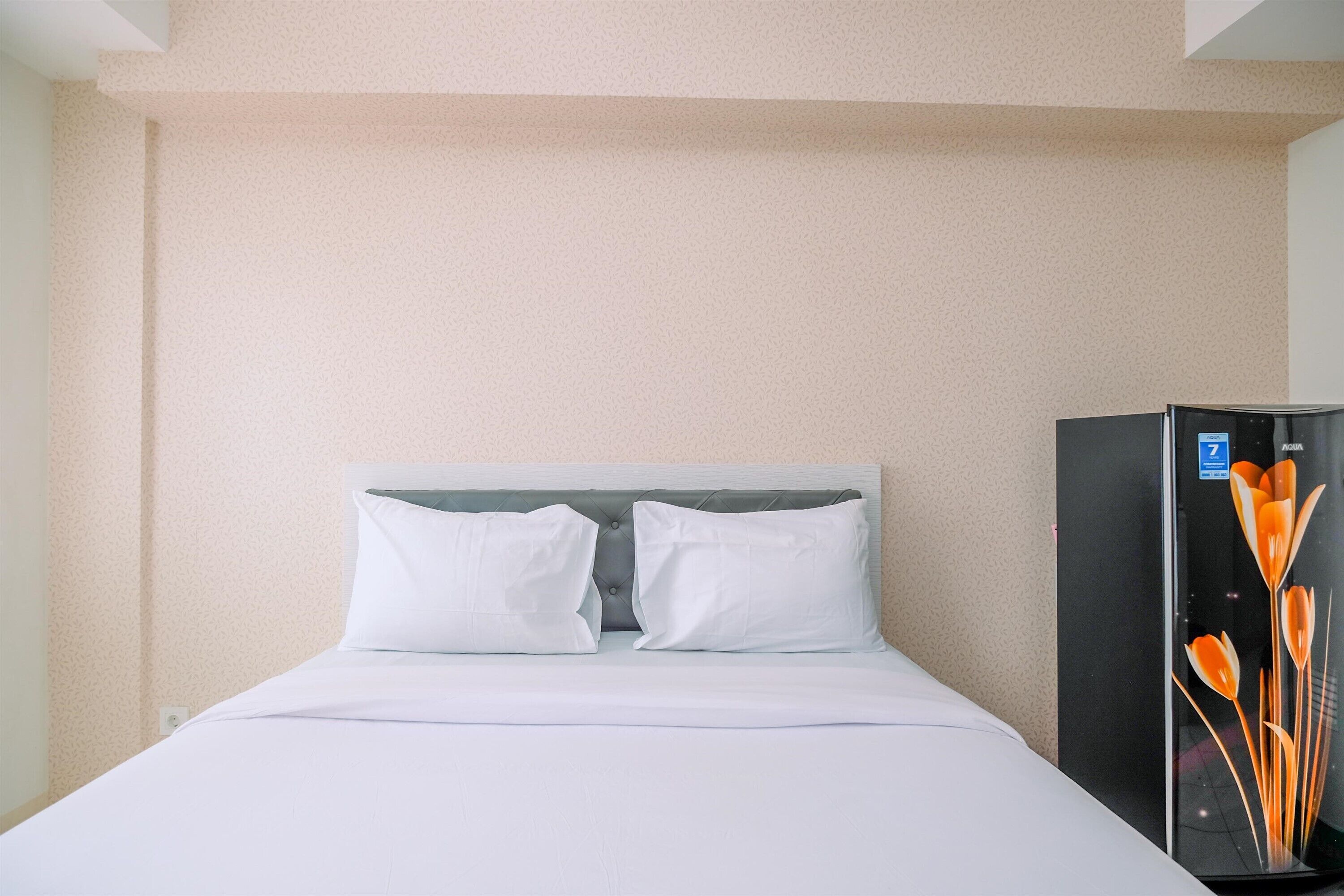 Ein Hotelzimmer mit einem Bett, zwei Kissen, einem Kopfteil und einem schwarzen Kühlschrank mit floralem Dekor.