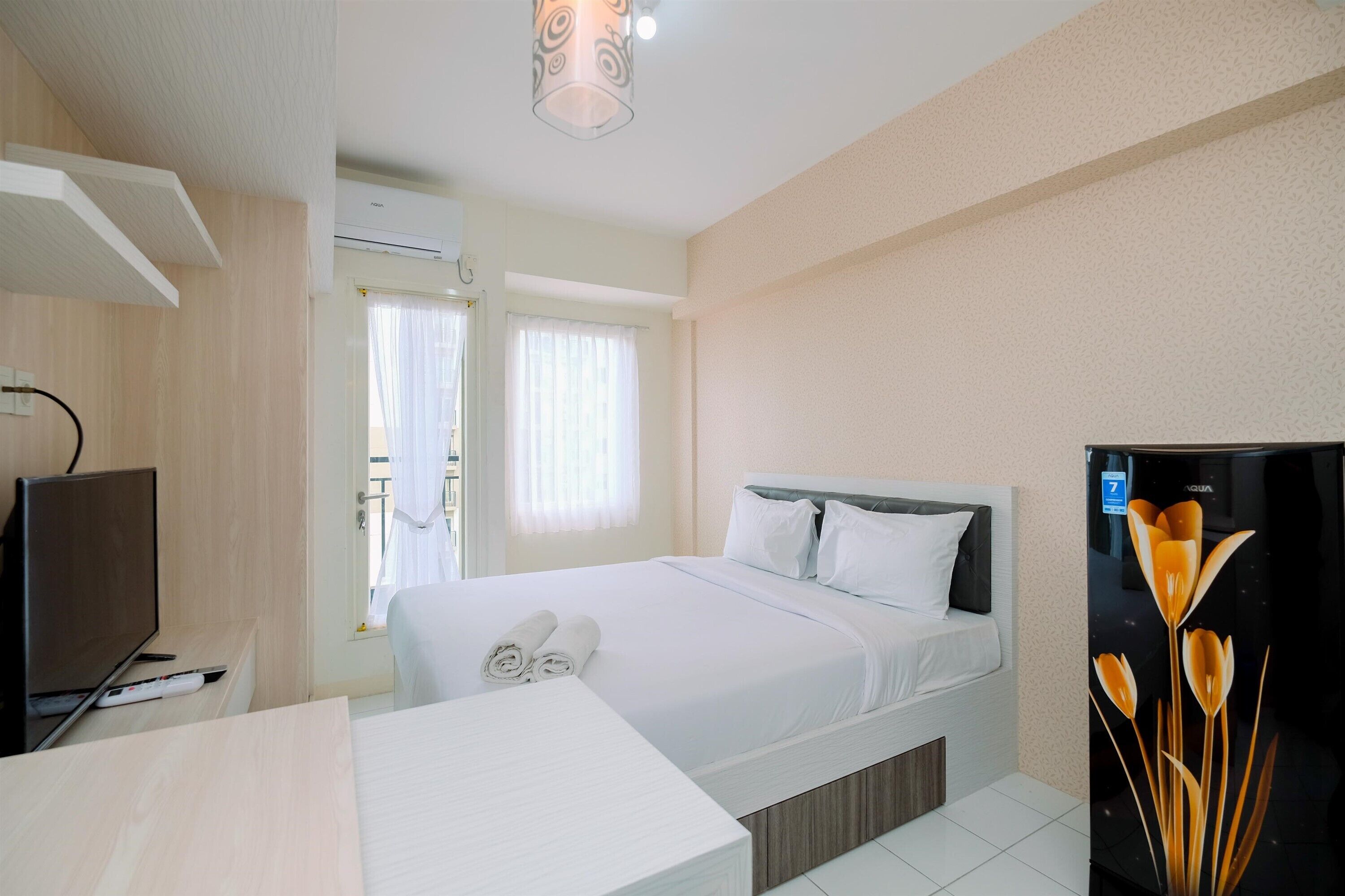 A hotel room with a bed, a TV, a desk, and a refrigerator.