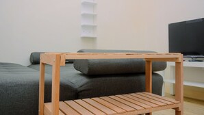 Een moderne woonkamer met een grijze bank, een houten salontafel en een televisie op een witte dressoir.