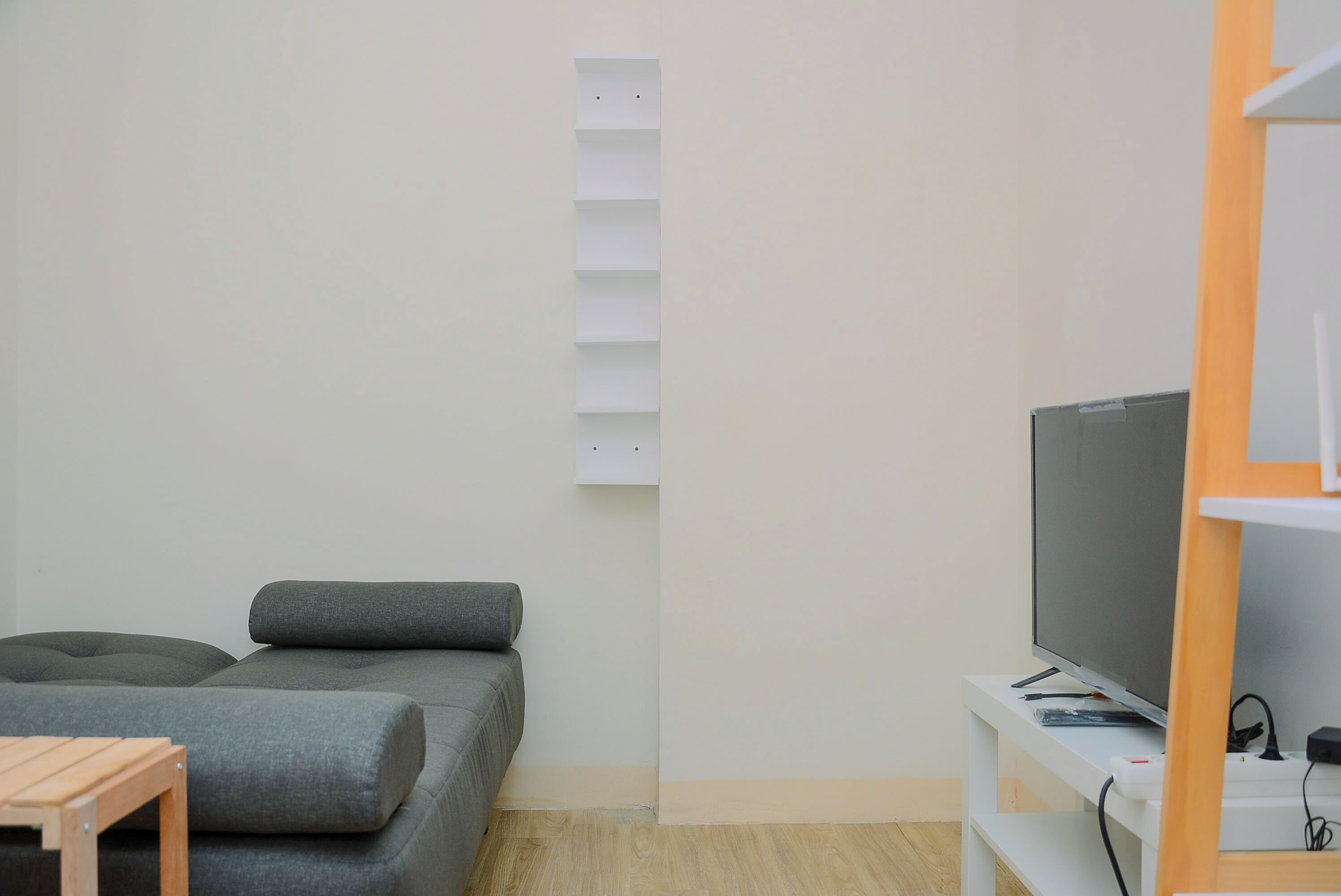 Uma sala de estar minimalista com um sofá cinzento, uma pequena mesa de madeira e uma televisão sobre um suporte branco.