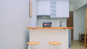 Een kleine keuken met witte kastjes, een zwarte afzuigkap en een aanrecht met twee houten stoelen.