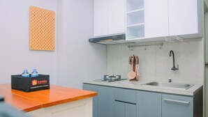 Een kleine keuken met een gasfornuis, spoelbak en een afzuigkap. Aan de muur hangt een houten prikbord en op het aanrecht staat een zwarte doos met flessen.