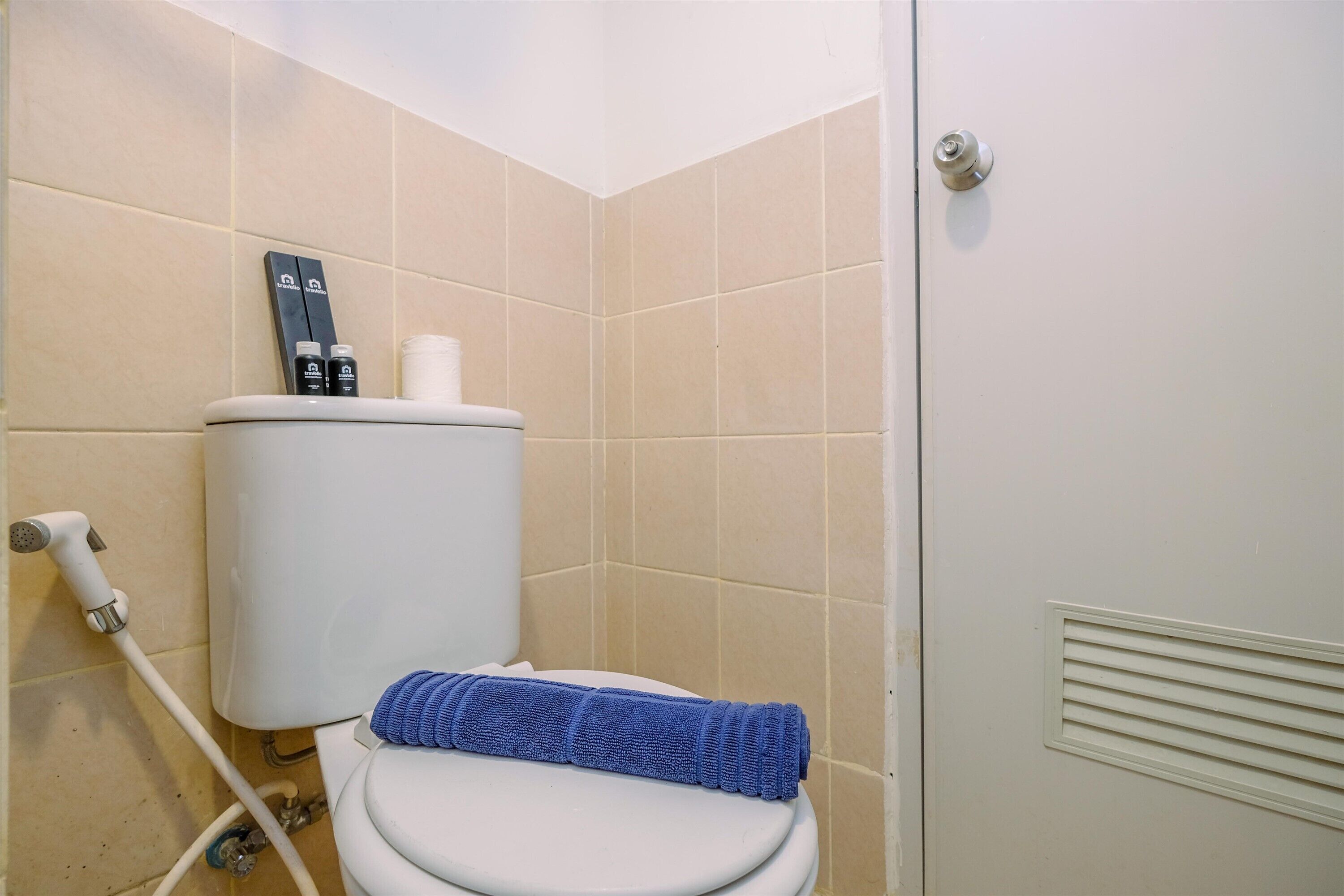 Une salle de bain avec des toilettes blanches, des carreaux beiges, une serviette bleue et un porte-rouleau de papier toilette.