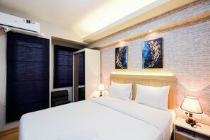 A hotel room with a bed, two bedside tables with lamps, a wardrobe, and a brick wall with two artworks. - Brand New and Fresh Studio Podomoro Golf View Apartment (Gunung Putri)