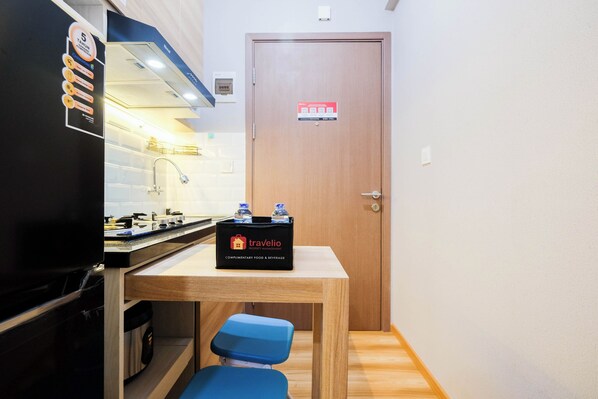 A compact kitchen with a refrigerator, sink, and a table with a travel bag. - Brand New and Fresh Studio Podomoro Golf View Apartment (Gunung Putri)