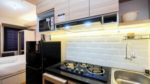 A modern kitchen with a black refrigerator, a stove, and a microwave. There is a sink and a cabinet above the stove. - Brand New and Fresh Studio Podomoro Golf View Apartment (Gunung Putri)