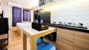 A compact hotel room with a kitchenette, a bed, a small table with a box of travel essentials, and a blue chair. - Brand New and Fresh Studio Podomoro Golf View Apartment (Gunung Putri)