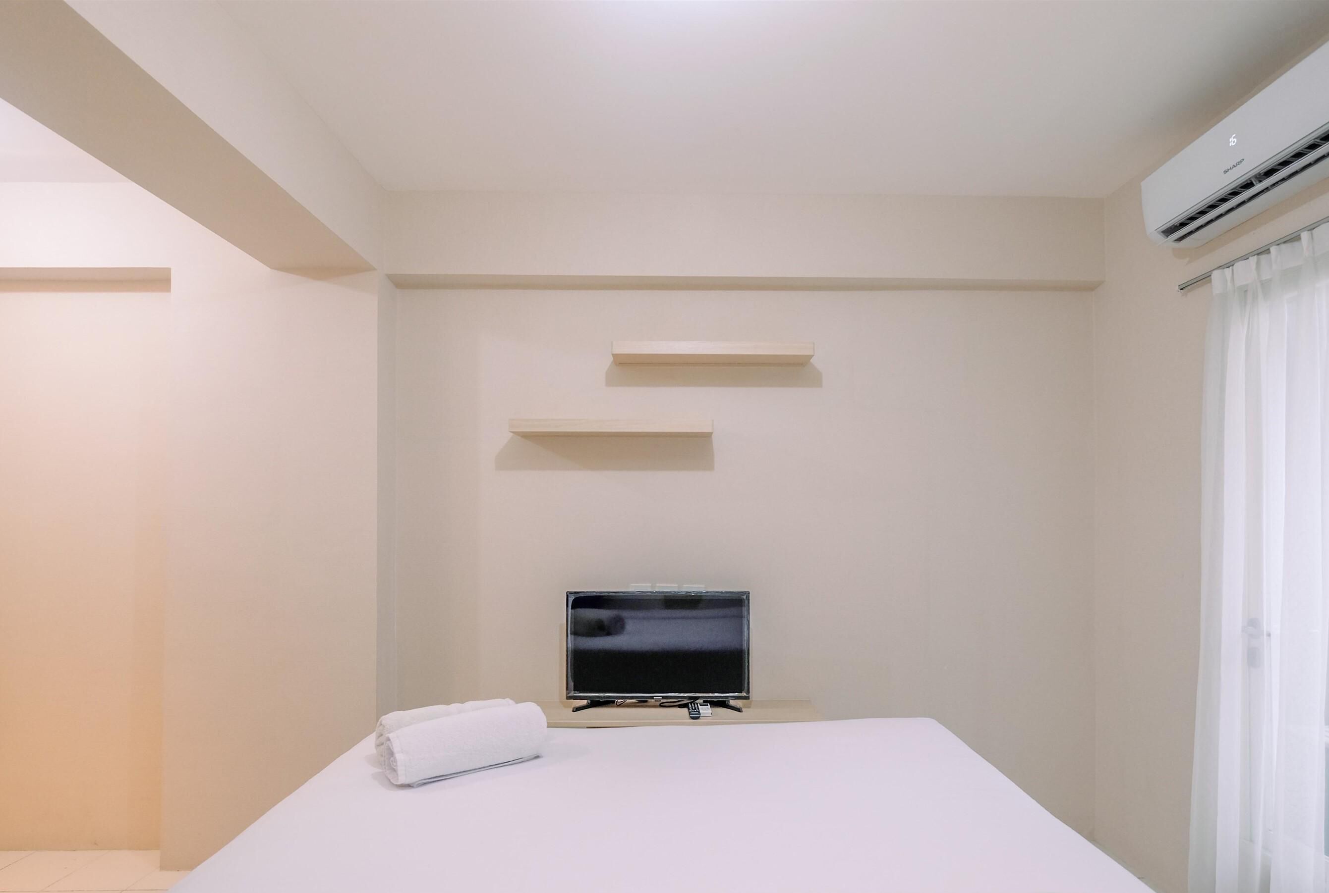 A hotel room with a bed, a flat-screen TV, a wall-mounted shelf, and an air conditioning unit.