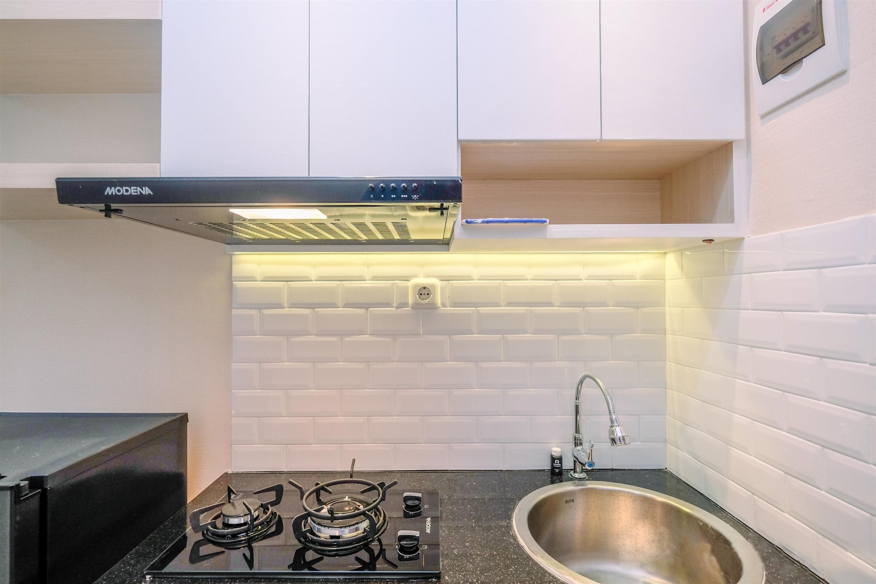 A compact kitchen with a gas stove, a stainless steel sink, and white tiled walls.
