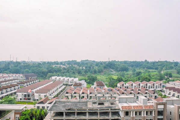 A residential area with modern apartment buildings, arranged in a grid pattern, with a green hillside in the background. - Nice and Warm 2BR at Podomoro Golf View Apartment (Gunung Putri)