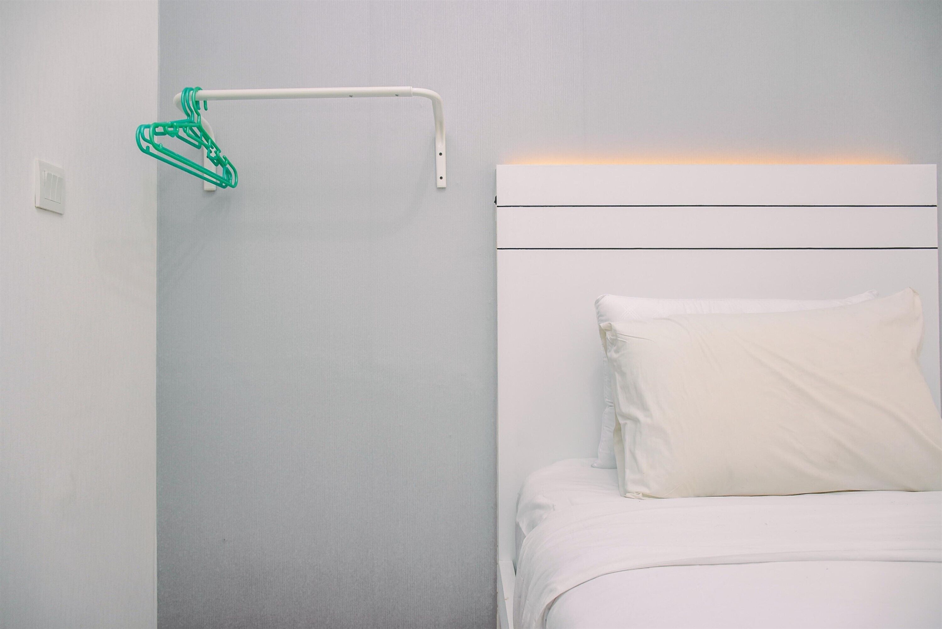 A white bed with a single white pillow in a room with a plain wall and a white headboard.
