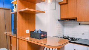 A modern kitchen with wooden cabinets, a glass countertop, and a built-in gas stove. - Nice and Warm 2BR at Podomoro Golf View Apartment (Gunung Putri)