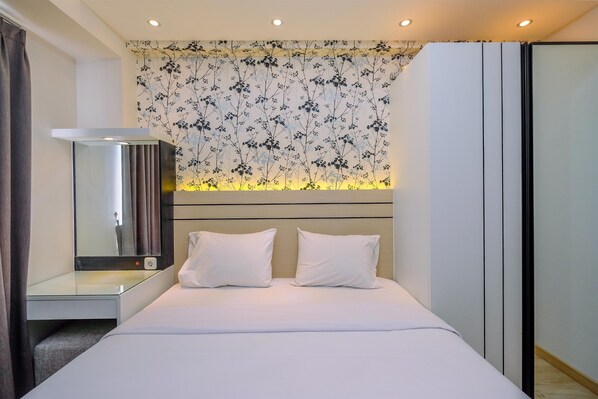 A modern hotel room with a bed, bedside table, and a large mirror. - Nice and Comfortable 2BR at Podomoro Golf View Apartment (Gunung Putri)
