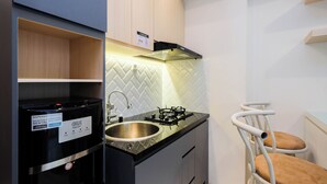 A compact kitchen with a black refrigerator, a sink, a gas stove, and a white chair.
