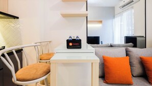A modern hotel room with a white desk, a chair, a sofa with orange cushions, and a minibar with bottled water.