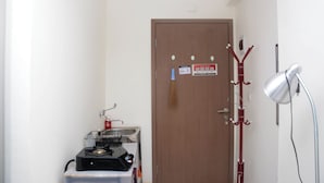 A room with a door, a coat rack, a lamp, and a small table with a kettle and a basket. - Comfort Studio Apartment for 4 Pax at Podomoro Golf View (Gunung Putri)