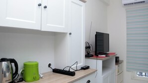 A small kitchenette with a kettle, a green coffee maker, a power strip, and a television on a wooden counter. - Comfort Studio Apartment for 4 Pax at Podomoro Golf View (Gunung Putri)