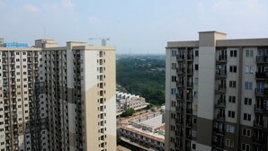 A high-rise residential building with multiple balconies and a view of a residential area in the background. - Comfort Studio Apartment for 4 Pax at Podomoro Golf View (Gunung Putri)