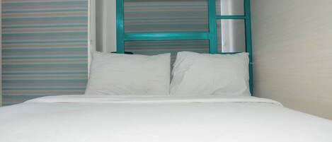 Una cama individual con ropa blanca y cabecera color turquesa.