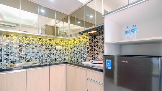A modern kitchen with a mosaic backsplash, stainless steel appliances, and wooden cabinets. - Comfortable and Tidy 2BR Podomoro Golf View Apartment (Gunung Putri)