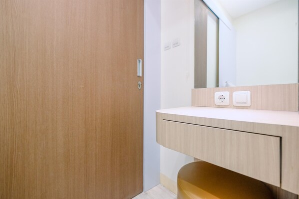 A modern bathroom with a wooden door, a light-colored vanity, and a mirror above it. - Comfortable and Tidy 2BR Podomoro Golf View Apartment (Gunung Putri)