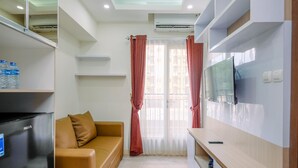 A modern room with a sofa, a TV mounted on the wall, a refrigerator, and a window with curtains. - Comfortable and Tidy 2BR Podomoro Golf View Apartment (Gunung Putri)