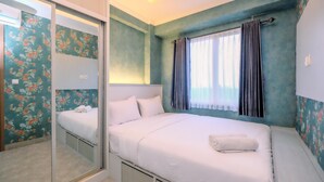 Une chambre à coucher avec un lit, un miroir, une fenêtre avec des rideaux et un papier peint à motifs floraux.