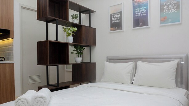 Een net opgemaakt bed met witte lakens en opgerolde handdoeken, een modern houten wandrek met potplanten, en motiverende posters aan de muur.