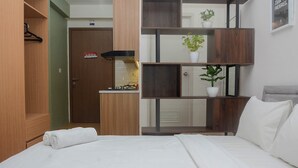 Een hotelkamer met een bed, een houten kledingkast, een kitchenette en een plank met planten.