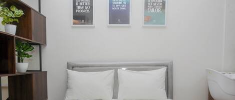 Una cama bien hecha con ropa de cama blanca, un cabecero gris y dos almohadas blancas. Hay tres carteles motivacionales enmarcados en la pared sobre la cama.