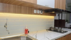 Een moderne keuken met houten kastjes, een witte marmeren aanrecht, een roestvrijstalen spoelbak, een gasfornuis en verlichting onder de kastjes.
