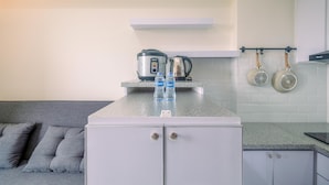 A modern kitchen with a grey countertop, a built-in oven, and a coffee maker. There are two kettles hanging on the wall and a pair of kettles on the countertop. - Fully Furnished with Cozy Design 2BR Podomoro Golf View Apartment (Gunung Putri)