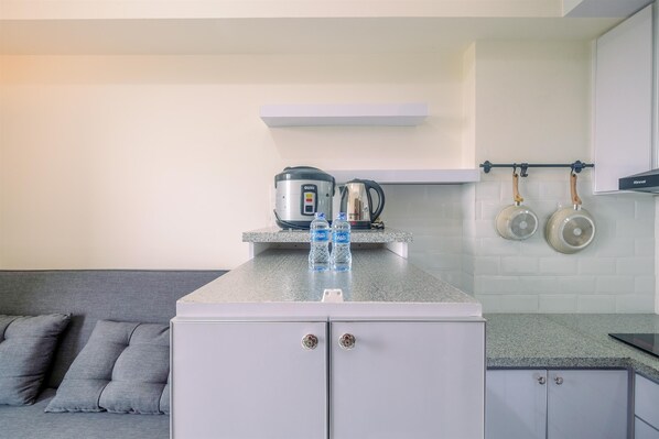 A modern kitchen with a grey countertop, a built-in oven, and a coffee maker. There are two kettles hanging on the wall and a pair of kettles on the countertop. - Fully Furnished with Cozy Design 2BR Podomoro Golf View Apartment (Gunung Putri)