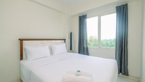 A hotel room with a large bed, a window with curtains, and a view of greenery outside. - Fully Furnished with Cozy Design 2BR Podomoro Golf View Apartment (Gunung Putri)