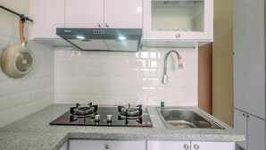 A kitchen with white cabinets, a gas stove, a microwave, and a stainless steel sink. - Fully Furnished with Cozy Design 2BR Podomoro Golf View Apartment (Gunung Putri)
