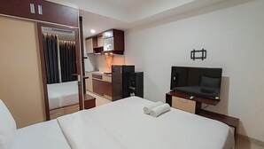 A hotel room with a bed, a TV, a desk, a wardrobe, and a kitchenette. - Brand New and Homey Studio at Tamansari Skylounge Makassar Apartment (Makassar)