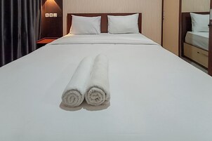 A neatly made bed with two rolled white towels in front, a wooden headboard, and a nightstand with a lamp.