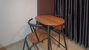 A corner of a room with a small wooden table and two chairs, a dark curtain, and a light-colored wall. - Brand New and Homey Studio at Tamansari Skylounge Makassar Apartment (Makassar)