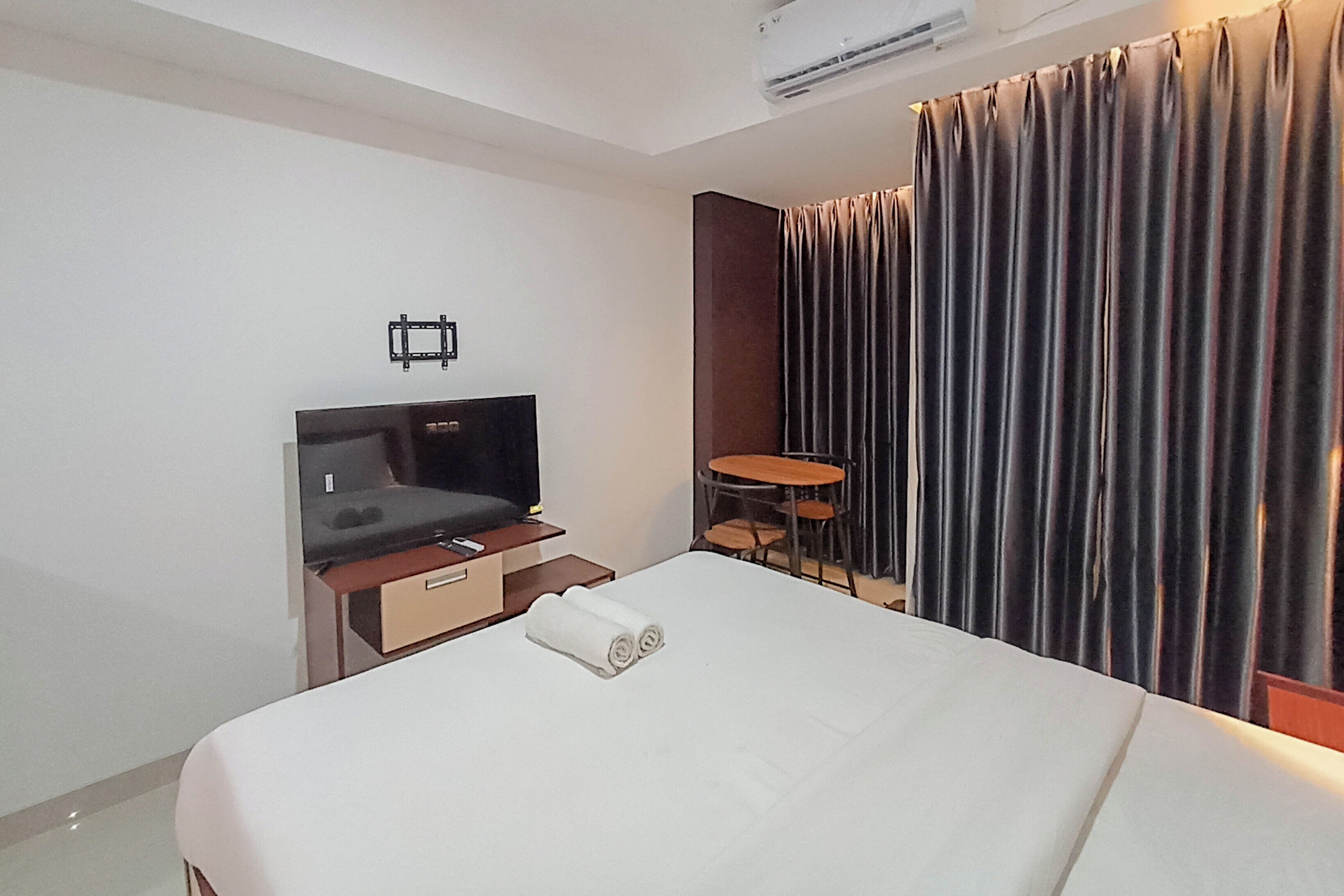 Una habitación de hotel con una cama, televisión, una mesita y una silla.
