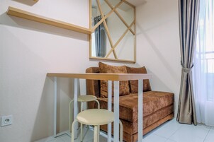Um quarto com um sofá marrom, uma mesinha branca e um espelho com moldura geométrica.