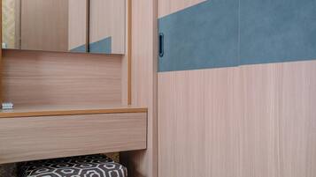 A bedroom with a wooden wardrobe, a bedside table, and a patterned ottoman.