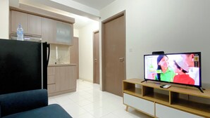 Een woonkamer met een televisie, een bank, een keukenhoek en een deur.