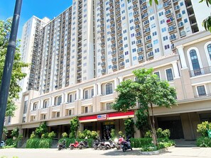 Um edifício residencial com vários andares, varandas, um andar térreo comercial e uma entrada arborizada.