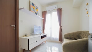 A modern living room with a white entertainment unit, a beige sofa, and a large window with curtains. - Cozy and Simply Look 2BR Podomoro Golf View Apartment (Gunung Putri)